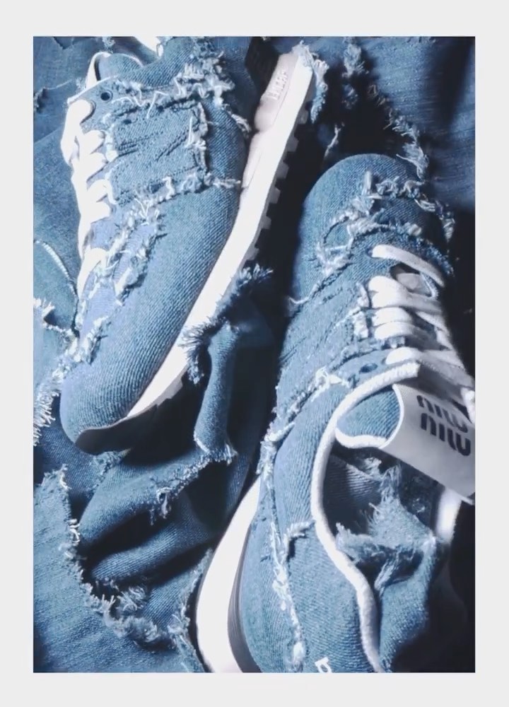 Denim sneakers with white laces and soles, surrounded by light blue denim fabric. Miu Miu logo visible on the side of one sneaker.