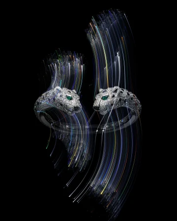 Two jaguar head rings with white gemstone embellishments are dynamically positioned against a black background with light streak accents.