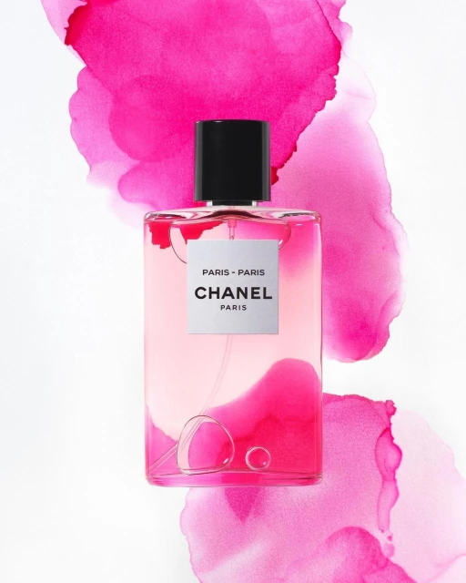 Chanel Paris-Paris perfume bottle on a white surface with abstract pink watercolor elements. Beauty, product shot, still life.