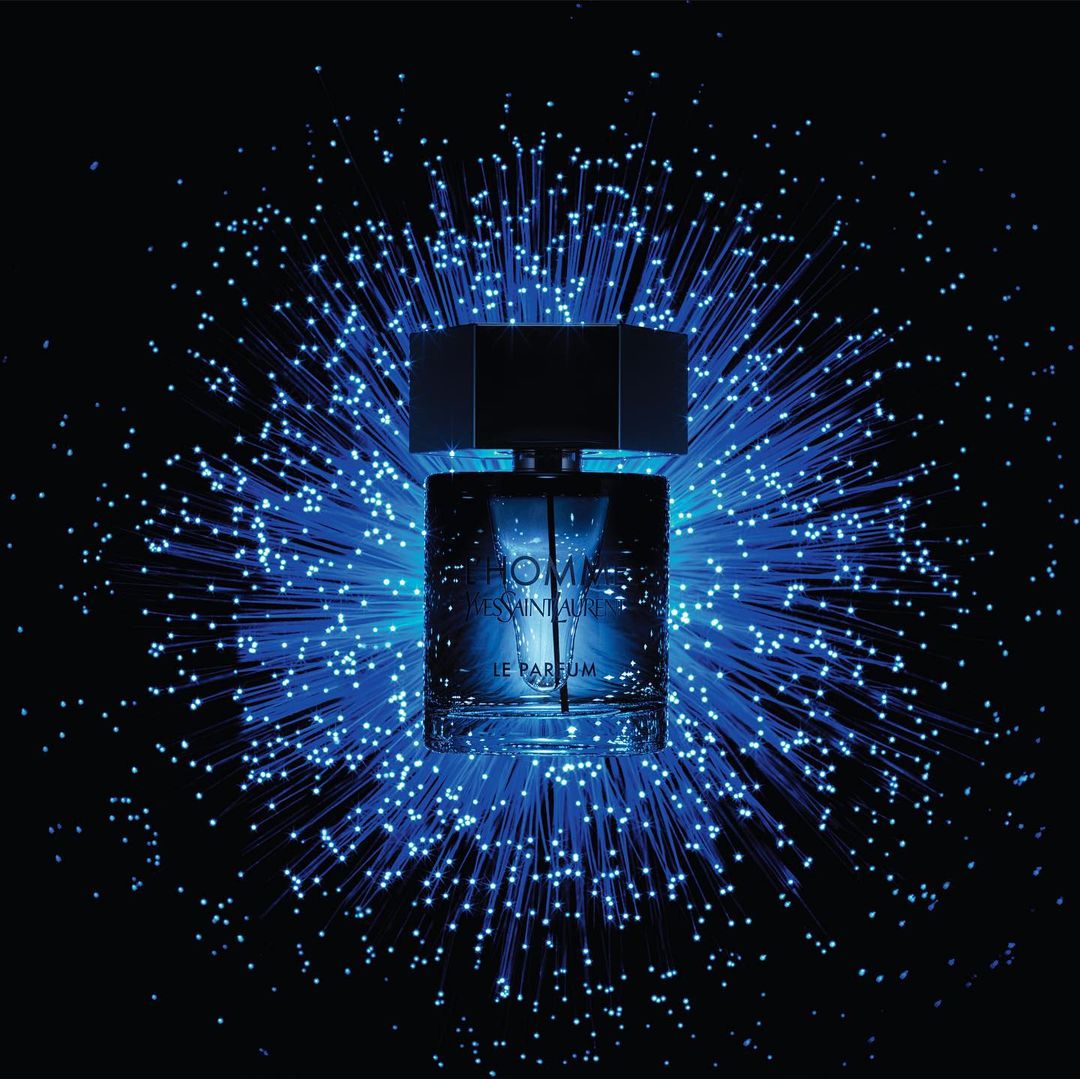 Cologne bottle of Yves Saint Laurent's Homme Le Parfum surrounded by blue fiber optic lights against a black background.