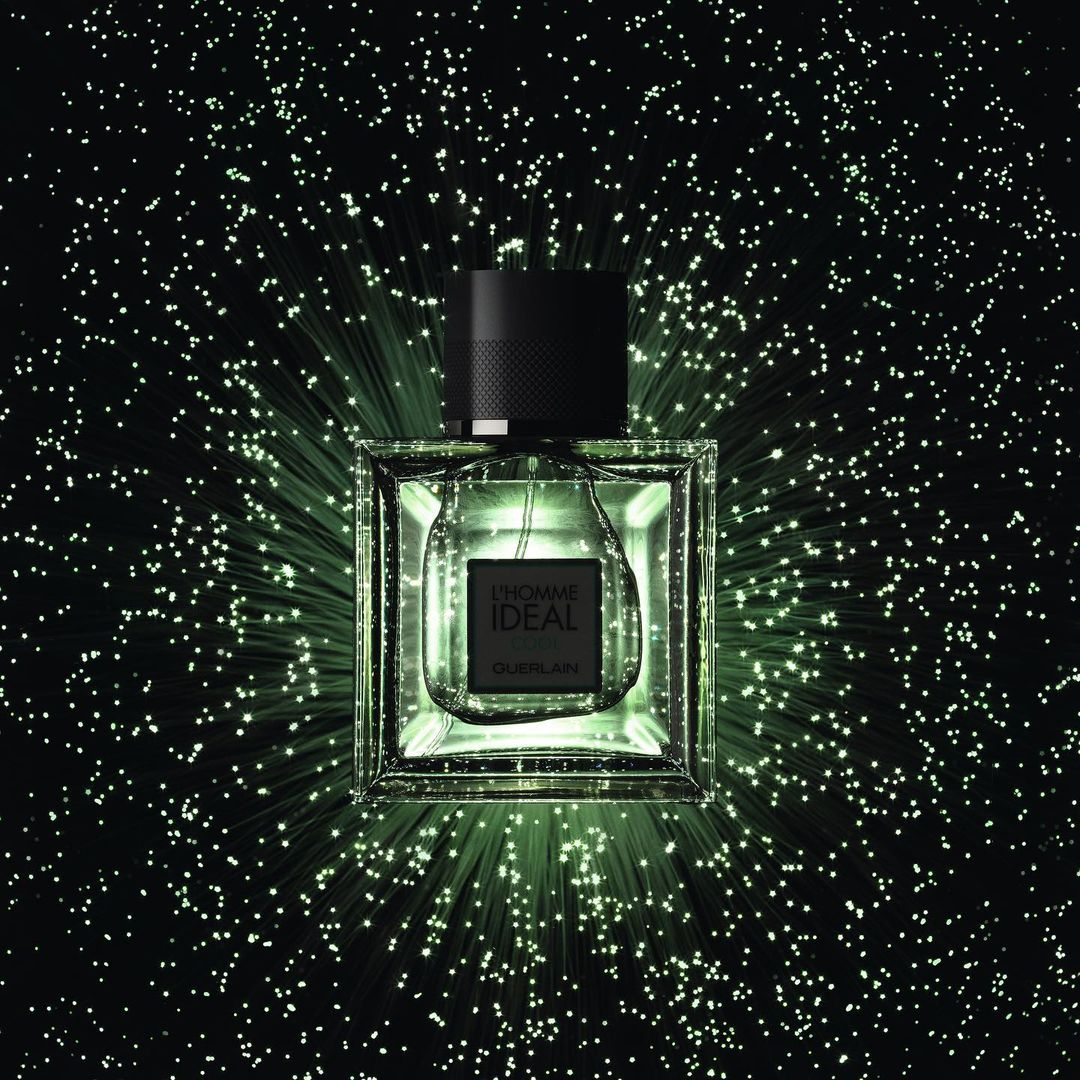 Square Guerlain L'Homme Idéal perfume bottle against a dark background with radiating green light effect and a black cap.