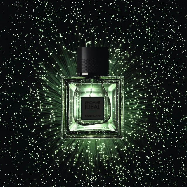 Square Guerlain L'Homme Idéal perfume bottle against a dark background with radiating green light effect and a black cap.