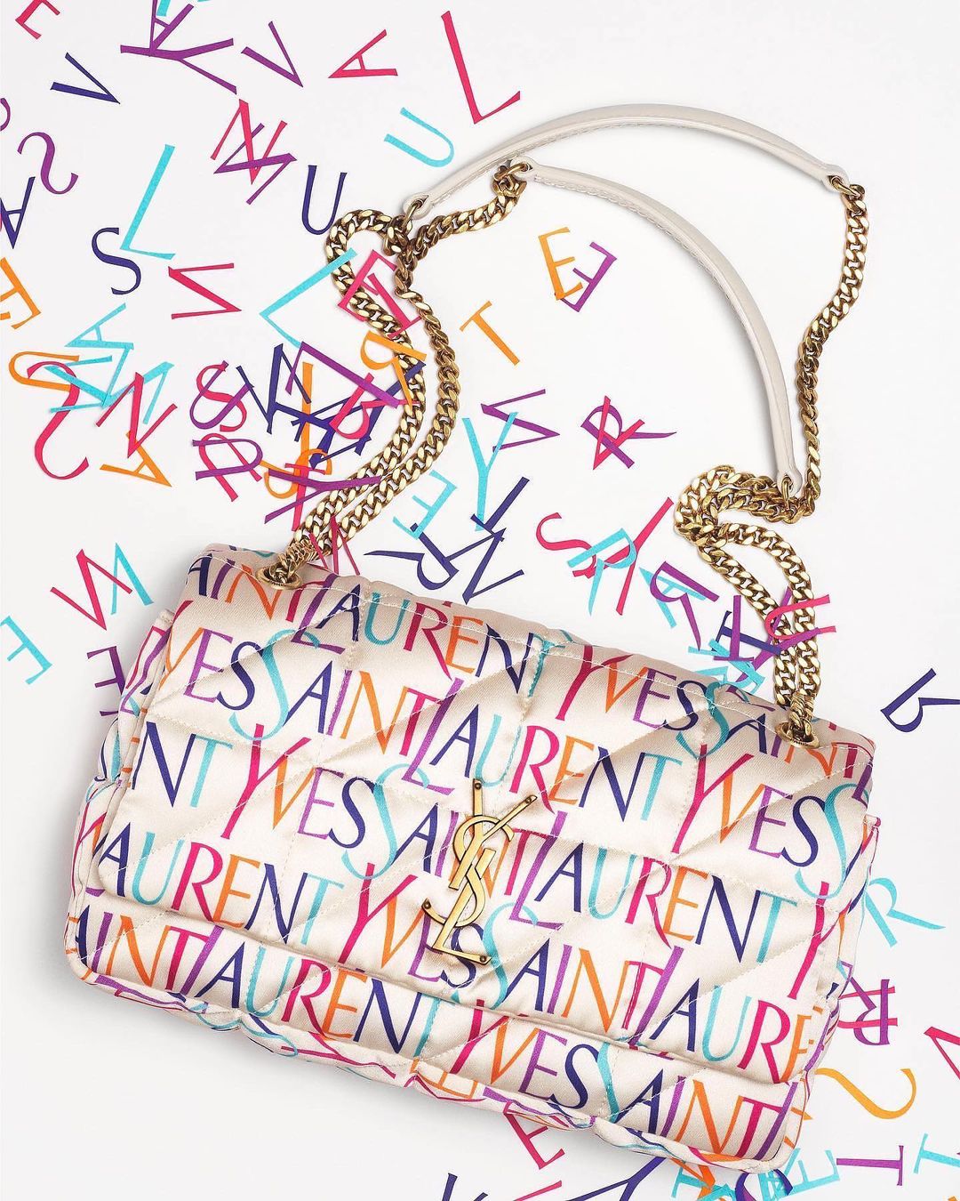 Cream quilted leather handbag with colorful Yves Saint Laurent brand typography print against white seamless background