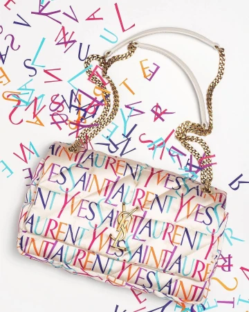 Cream quilted leather handbag with colorful Yves Saint Laurent brand typography print against white seamless background