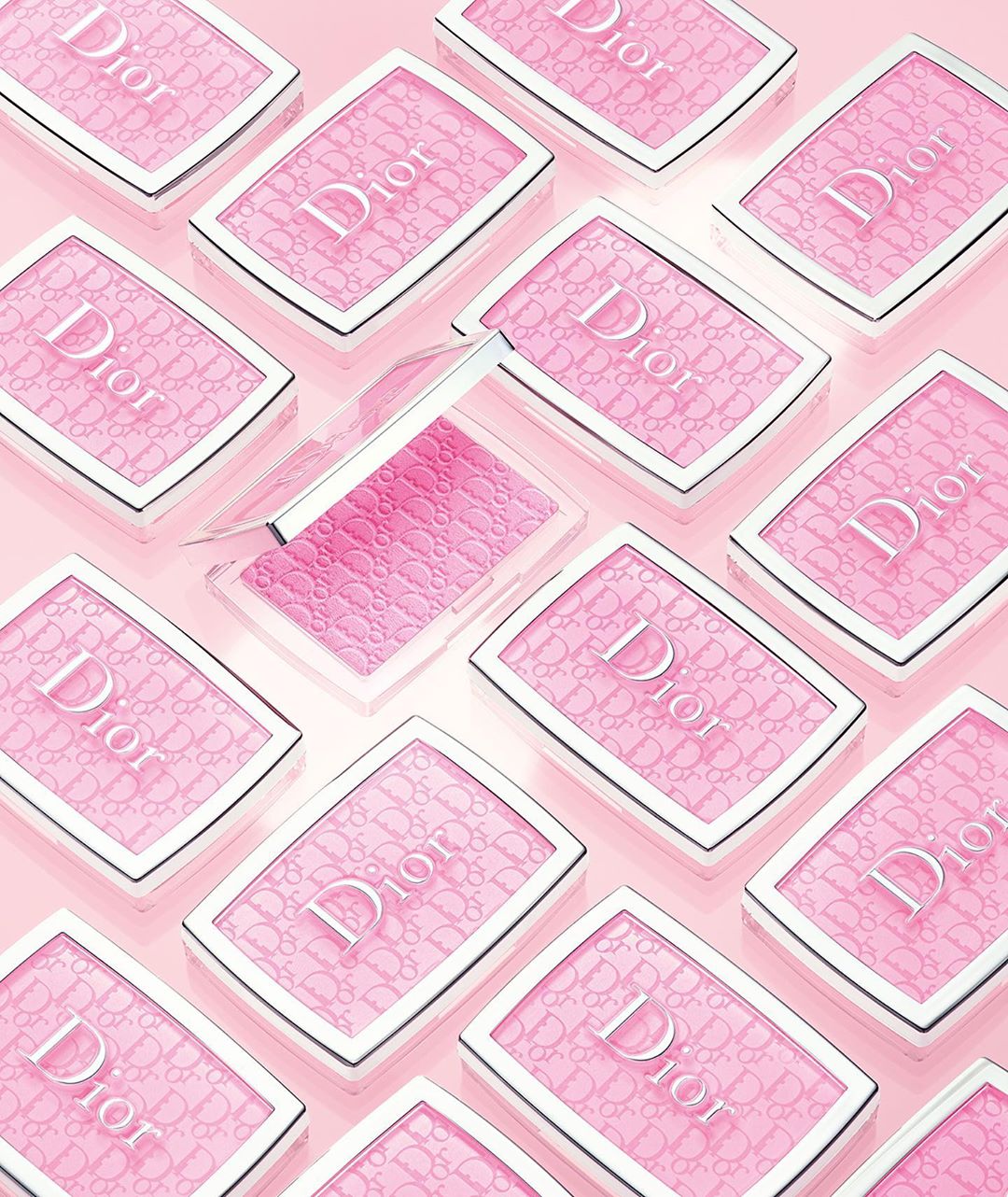 Overhead shot of multiple Dior blush compacts in a light pink hue, neatly arranged on a matching light pink surface.