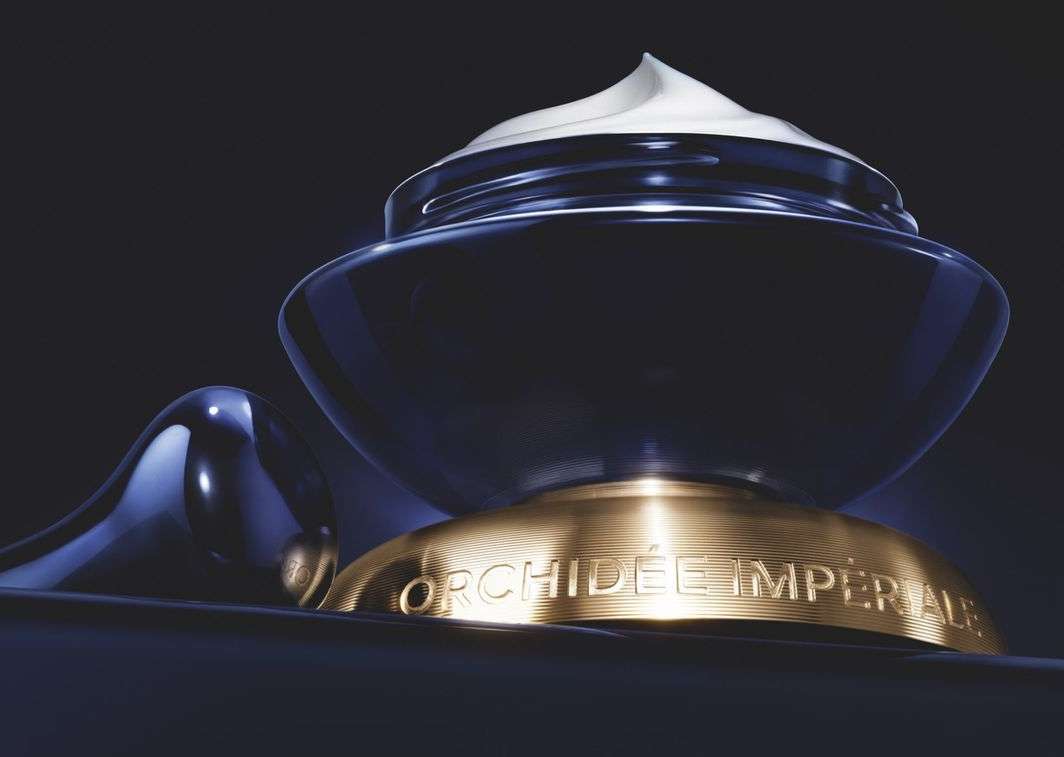 Elegant dark blue cosmetic cream jar with a gold base, filled with white cream, presented against a solid dark background.