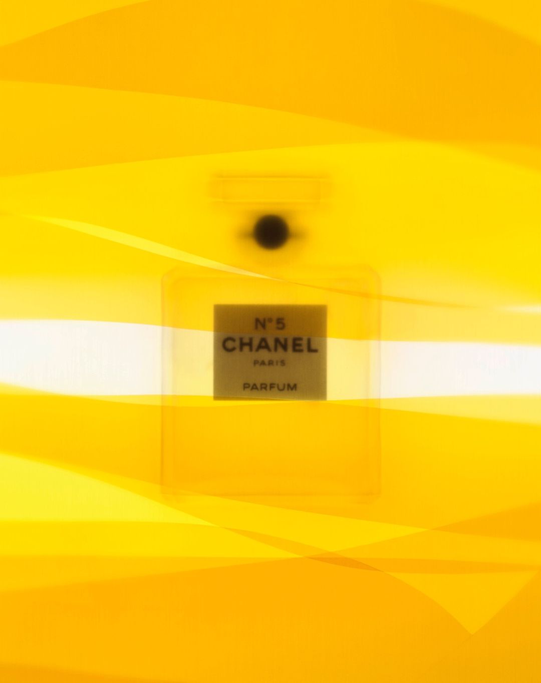 Close-up studio shot of a transparent Chanel N°5 perfume bottle against a yellow background, emphasizing its design and brand.