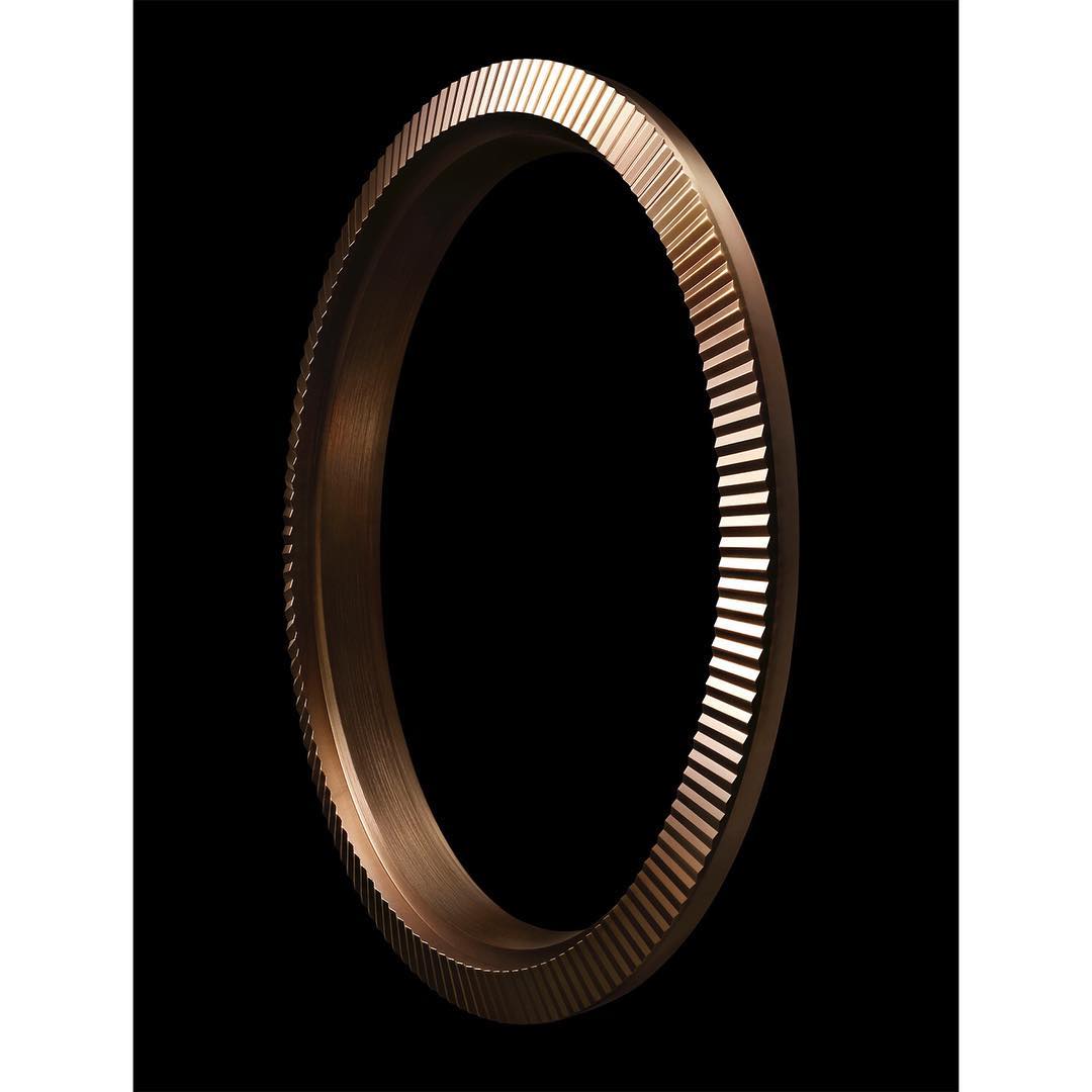 Close-up of a bronze metal ring with linear indentations. The metallic ring, set against a black background, showcases industrial design.