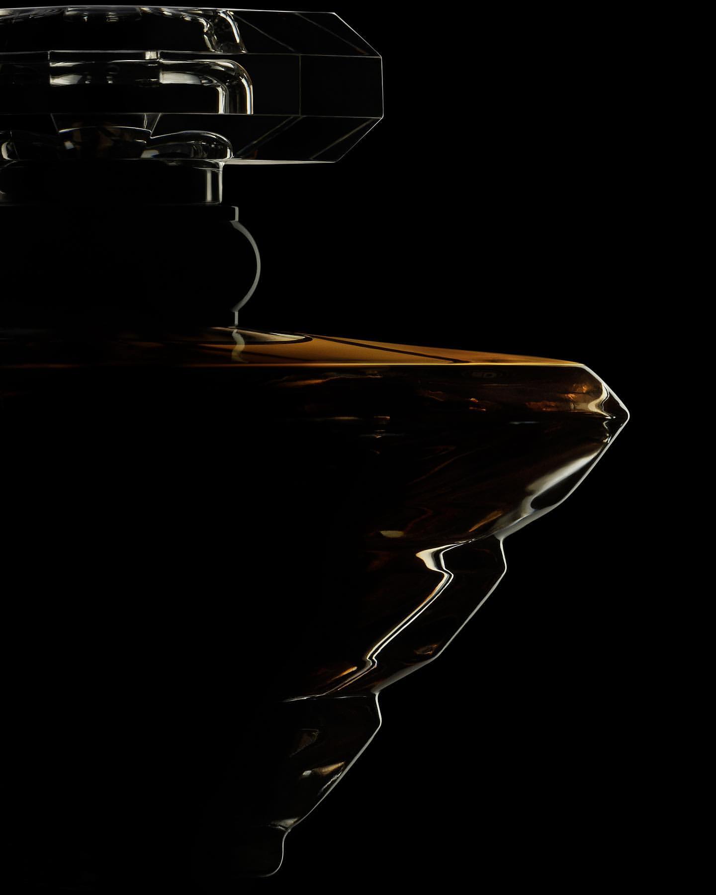 Dramatic product shot of a dark amber glass perfume bottle against a stark black background, showcasing geometric cap and reflective surface.
