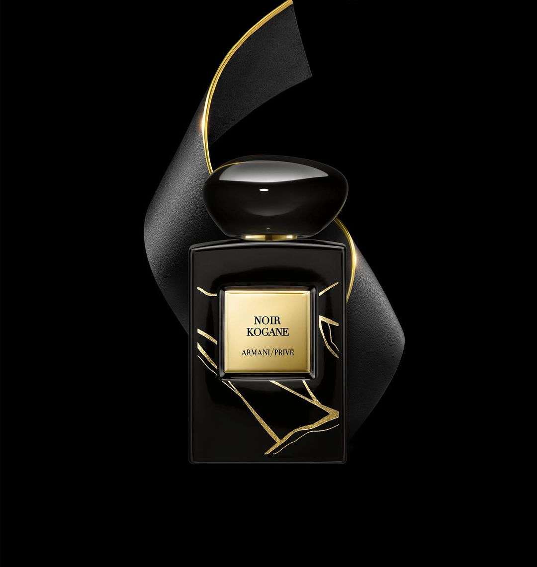 Elegant studio shot of a black glass Armani perfume bottle accented with gold, set against a dark background and flowing black ribbon.