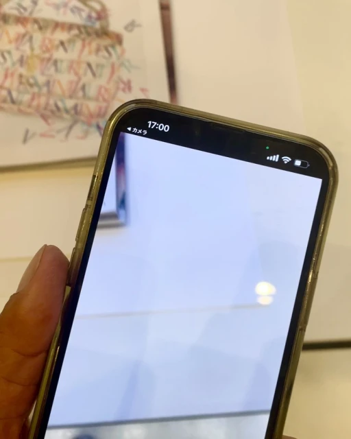 Image of a cellphone displaying a mostly white screen with top bar details such as time and battery life visible; object on table.