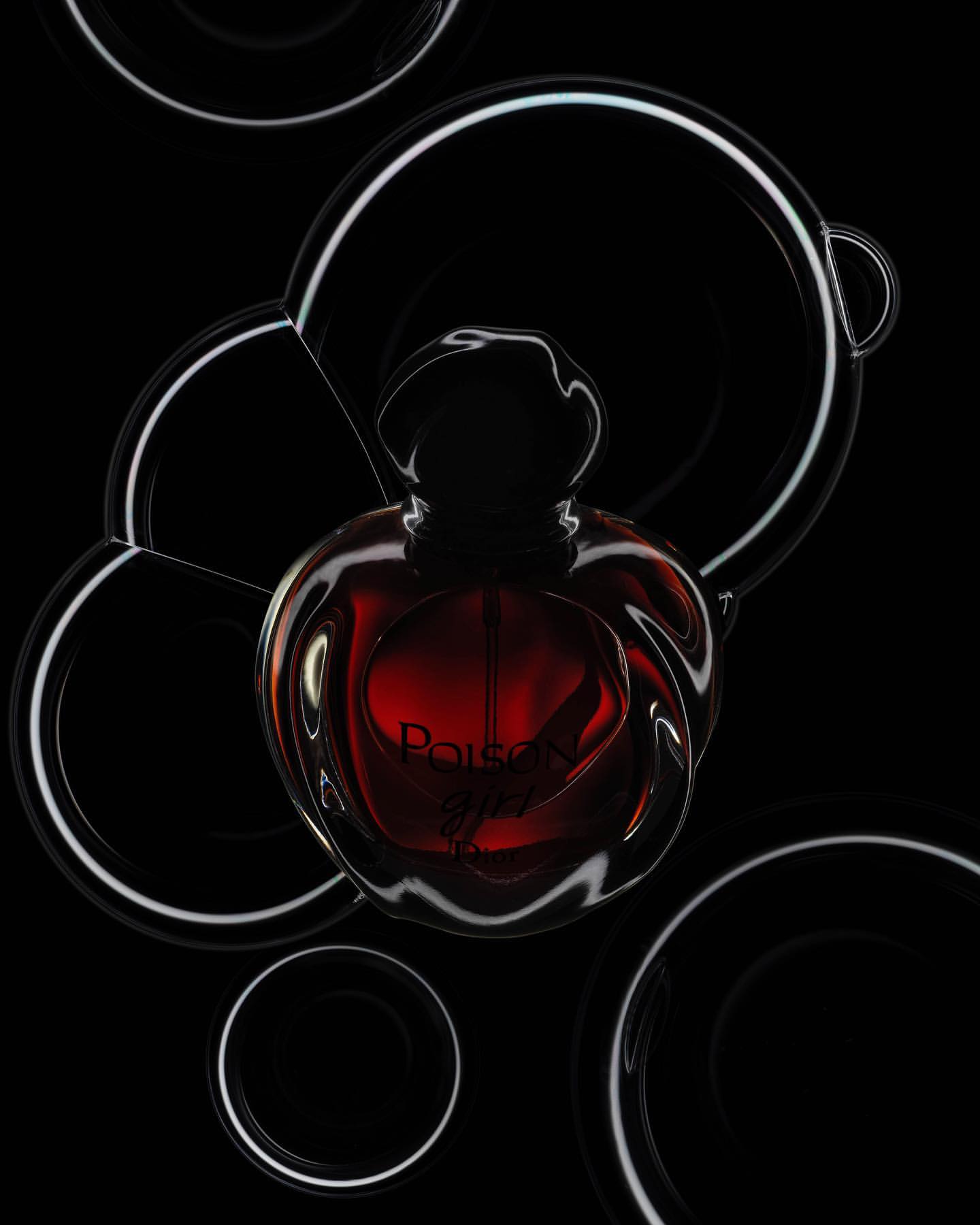 Elegant studio shot of a 'Poison Girl' perfume bottle surrounded by decorative black and white rings against a dark background.