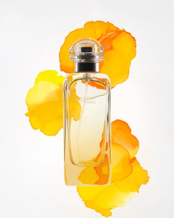Perfume bottle by Hermès, Un Jardin à Cythère fragrance, clear glass with gold liquid, surrounded by orange watercolor splashes on white.