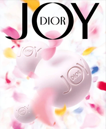 JOY by Dior advertisement featuring two perfume spheres with colorful flower petals falling around them on a white background.
