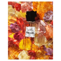 A rectangular glass perfume bottle with a black cap resting on a vibrant background of colorful textured sea shells.