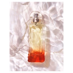 Glass perfume bottle with amber and orange gradient liquid resting against rippling water reflections