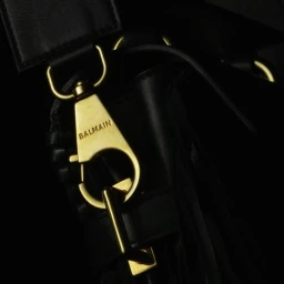 Close up of a black leather handbag featuring polished gold hardware and a branded clasp stamped with Balmain.
