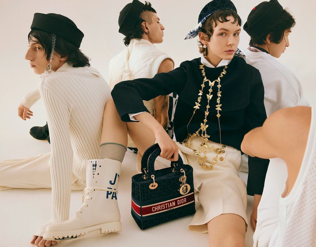 Fashion editorial shot with five people wearing modern clothing and accessories in a light studio, showcasing high-end apparel and accessories.