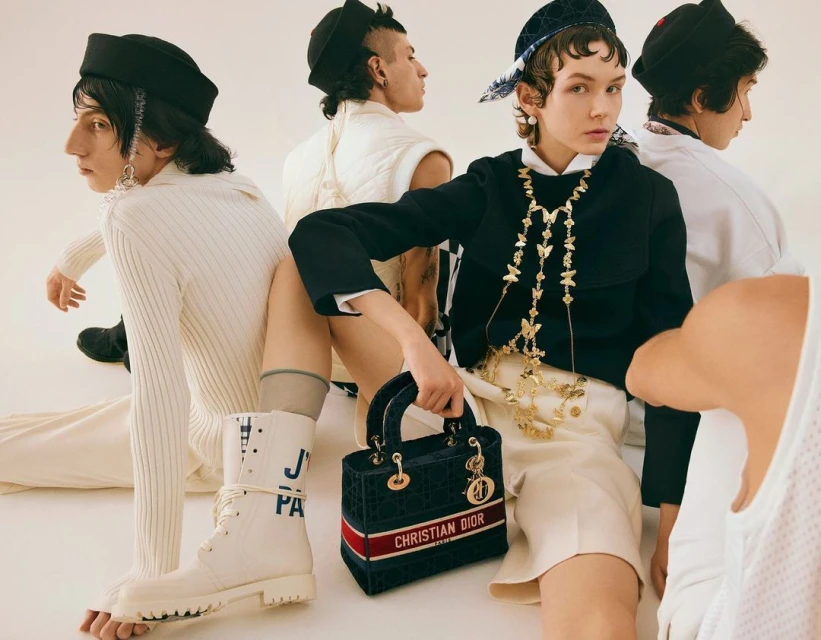 Fashion editorial shot with five people wearing modern clothing and accessories in a light studio, showcasing high-end apparel and accessories.