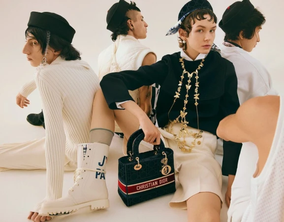 Fashion editorial shot with five people wearing modern clothing and accessories in a light studio, showcasing high-end apparel and accessories.