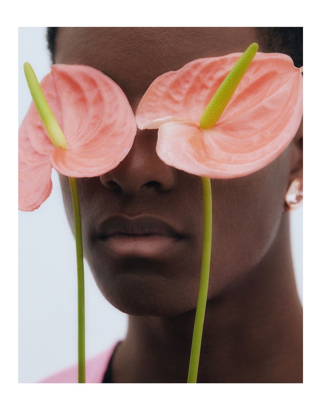 Close-up of an African American person with two pink Anthurium flowers covering the eyes, creating an artistic, abstract beauty image.