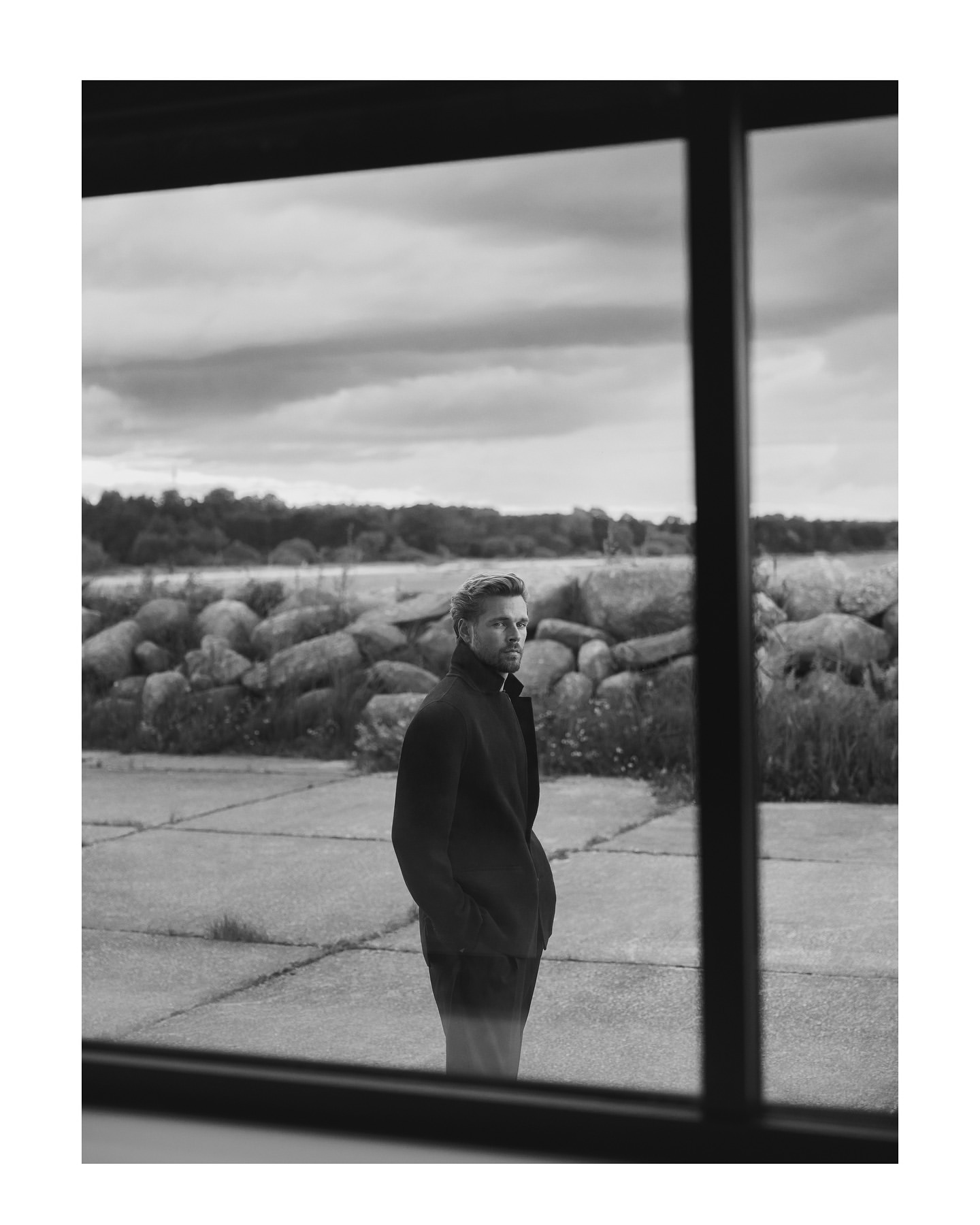 Man standing outdoors viewed through a large window, wearing a dark jacket in Istanbul by Koray Parlak.