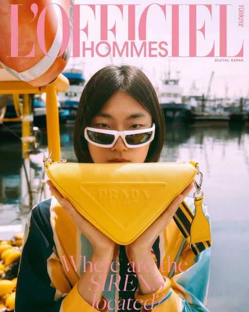 Magazine cover of a woman holding a Prada handbag with a harbor and boats in the background, featuring L'Officiel Hommes Türkiye.