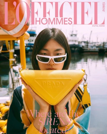 Magazine cover of a woman holding a Prada handbag with a harbor and boats in the background, featuring L'Officiel Hommes Türkiye.