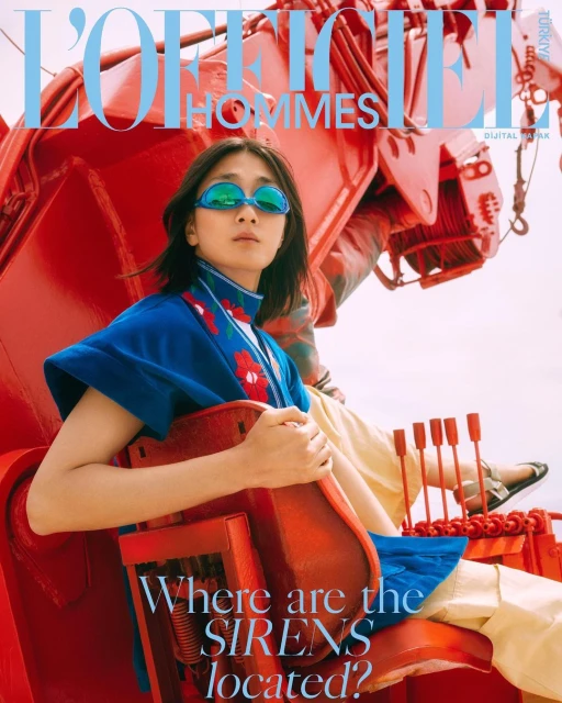 Fashion editorial image features an Asian woman wearing teal glasses and a floral kimono in a vibrant red industrial setting.