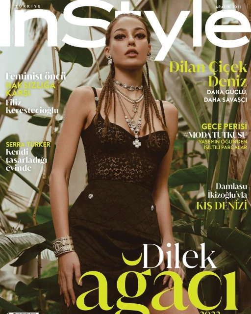 Magazine cover featuring Dilan Çiçek Deniz, posing in a black dress with layered necklaces, with a background of green plants.