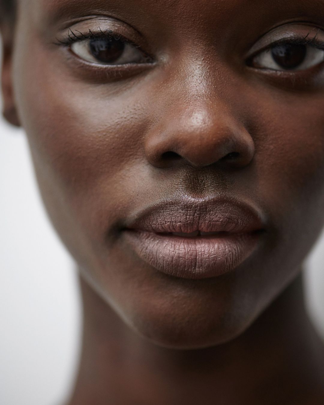 Close-up portrait of an African American woman with dark skin, glossy lips, and brown eyes, against a plain white background. Beauty shot.