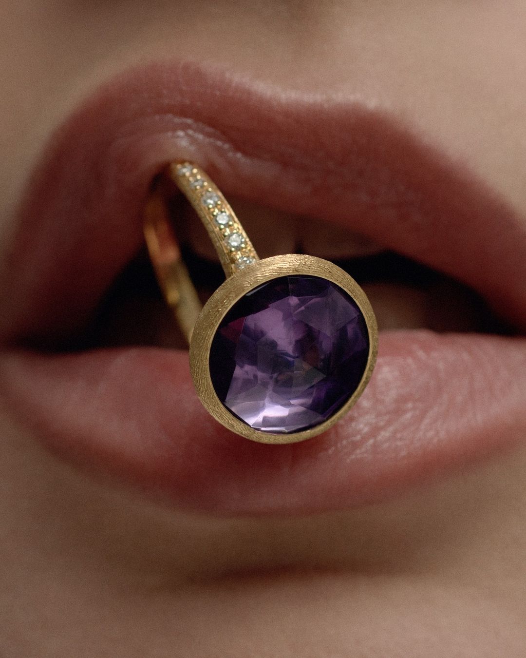 Close-up studio shot of a golden ring with an amethyst held in a person's mouth showcasing jewelry, beauty, and high-end luxury.