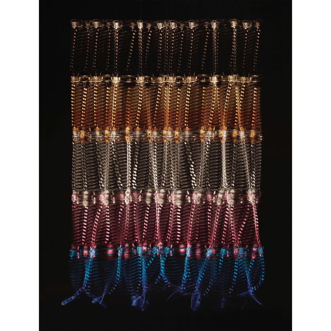 Abstract art with rows of hanging, colorful, string-like decorations against a black backdrop, creating a textured and patterned effect.