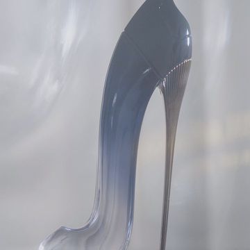 Elegant and sleek stiletto heel perfume bottle in light blue and silver tones, displayed against a neutral blurred backdrop.