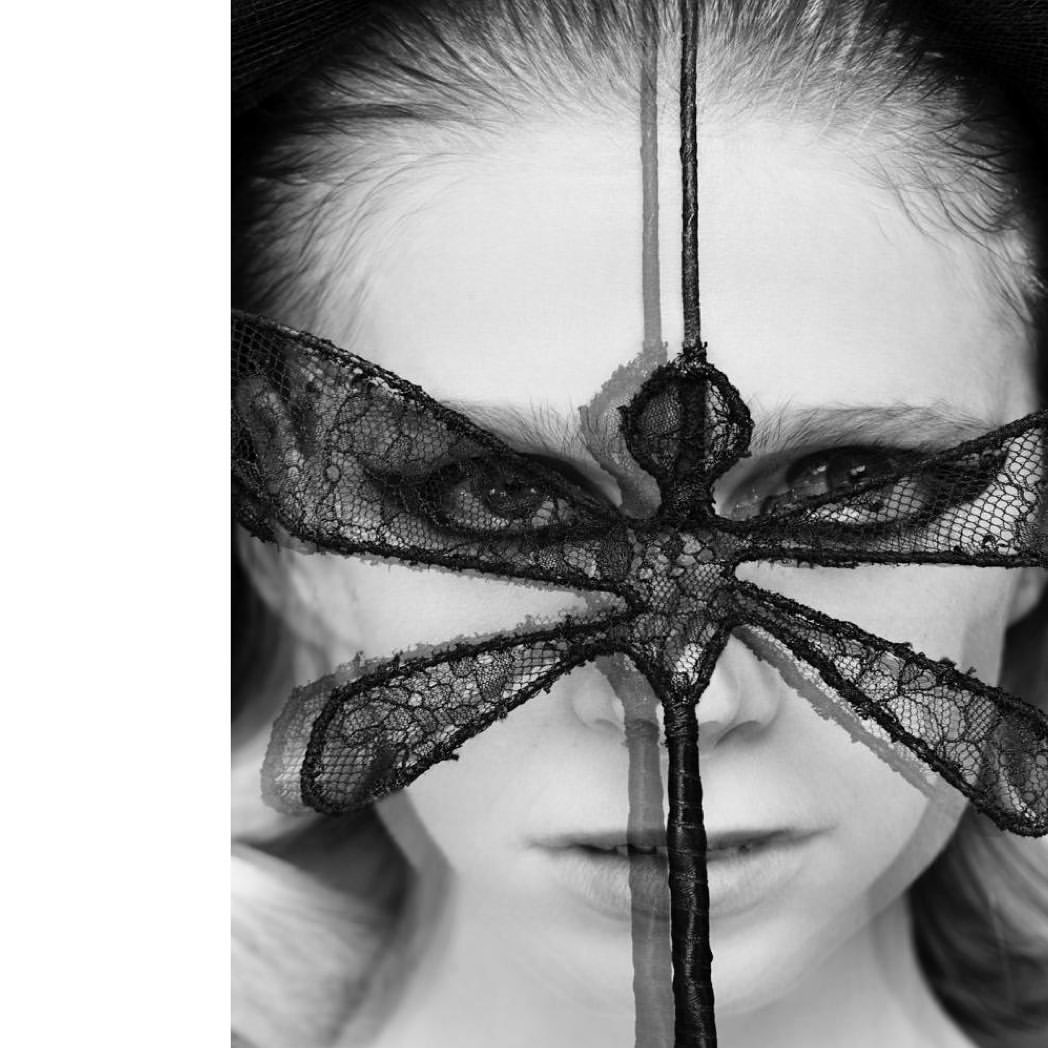 Monochrome portrait of a person wearing a black lace mask with a dragonfly design, creating a dramatic and artistic close-up.