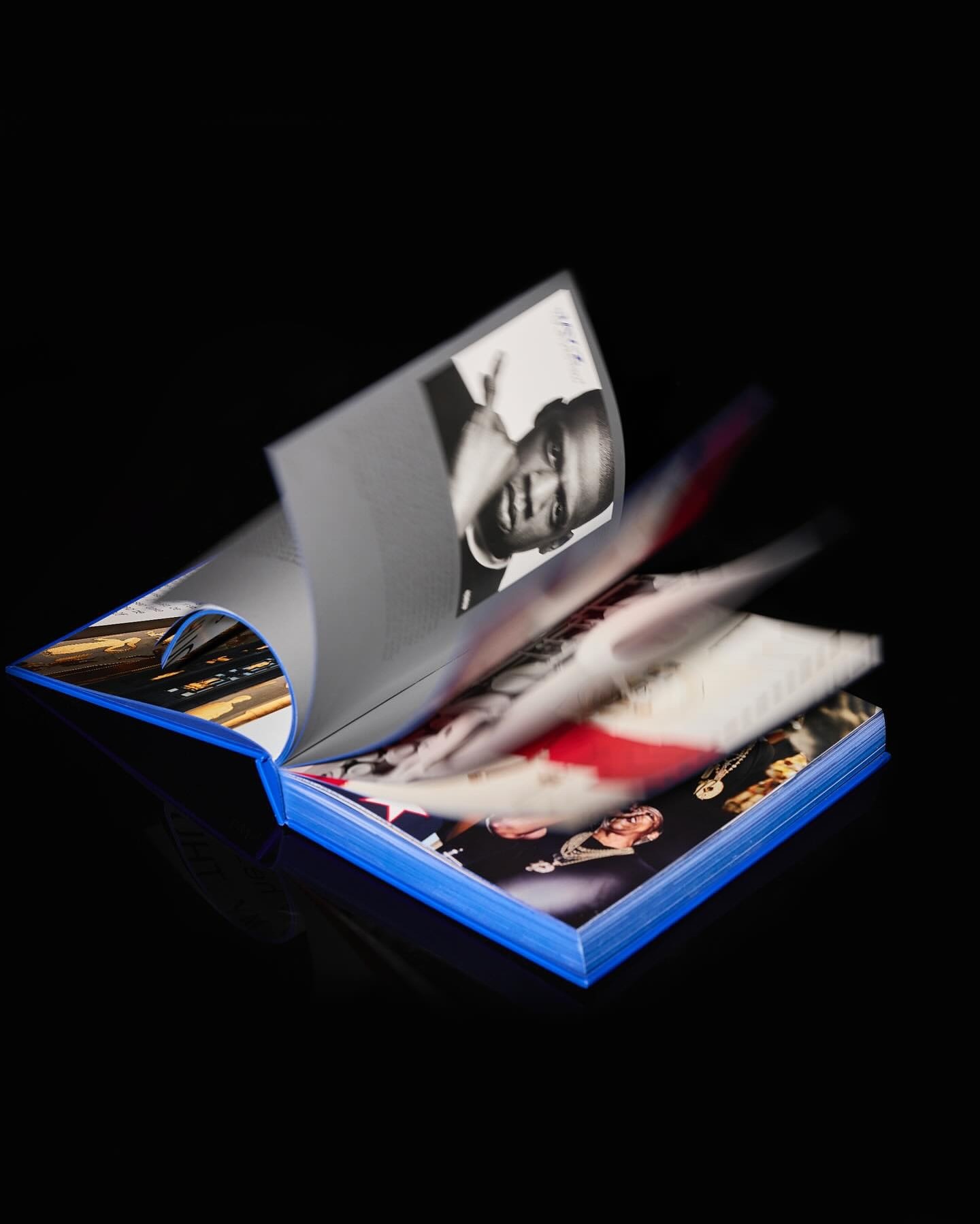 Open book with blue cover and pages showing various photos, including a black-and-white portrait, against a solid black background.