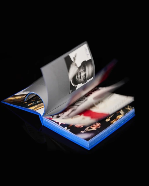 Open book with blue cover and pages showing various photos, including a black-and-white portrait, against a solid black background.