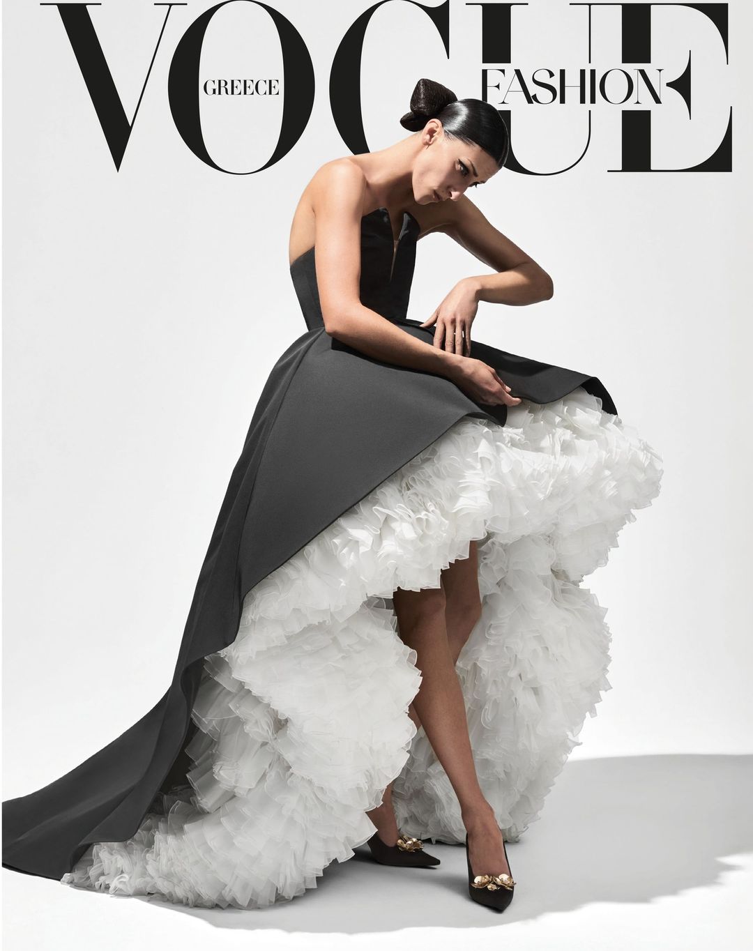 Vogue Greece cover featuring a fashion model in an elegant black and white gown posing in a photo studio with bright, soft lighting.