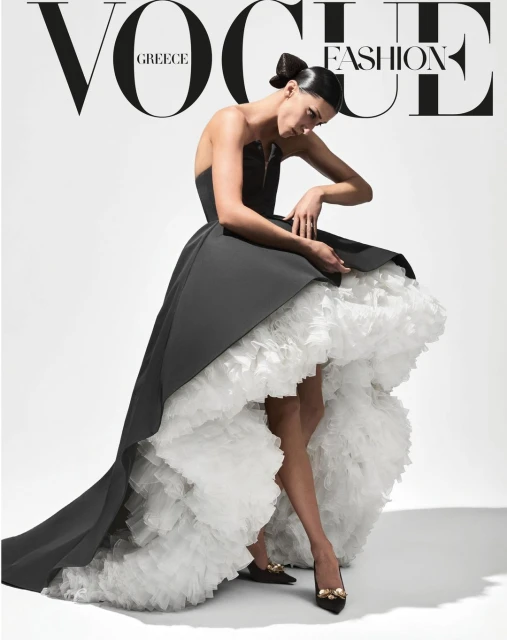 Vogue Greece cover featuring a fashion model in an elegant black and white gown posing in a photo studio with bright, soft lighting.