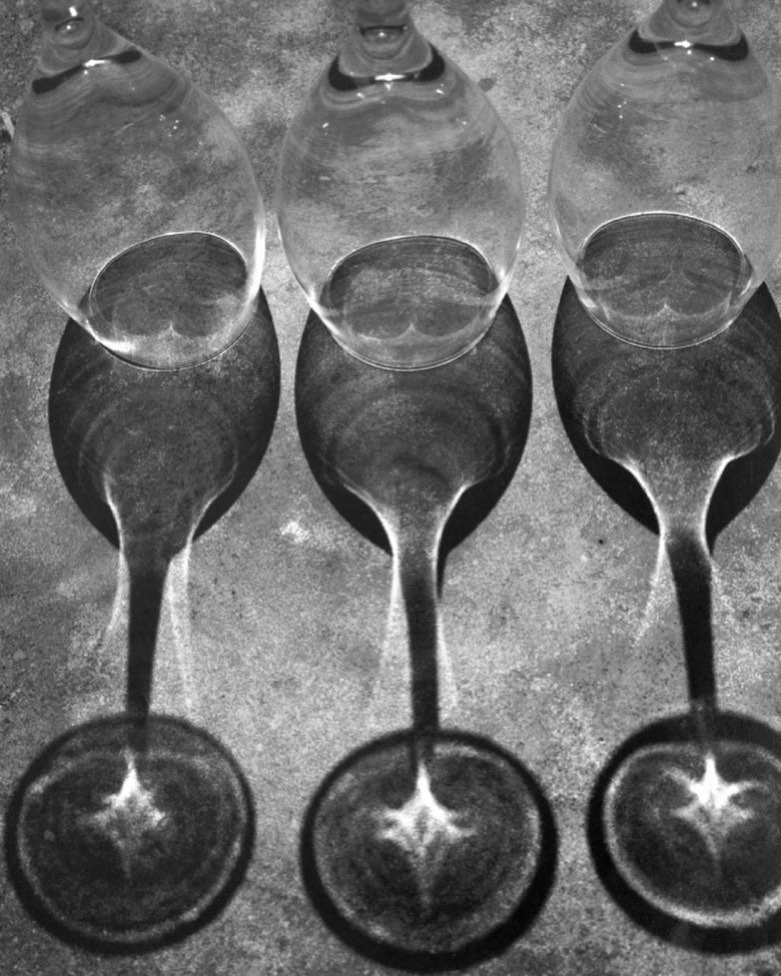 Monochromatic studio shot of three empty wine glasses casting strong shadows, creating an abstract and visually intriguing composition.