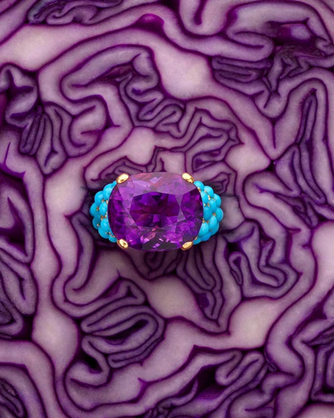 Macro shot of a ring with a large amethyst and turquoise stones set on gold band, placed on the texture of a red cabbage.