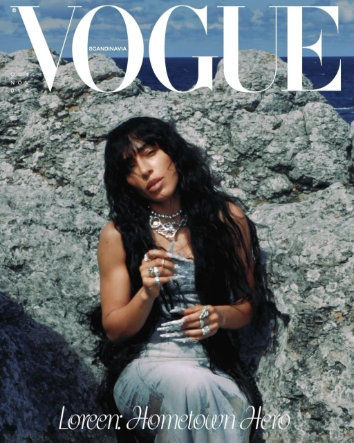 Vogue cover featuring a woman with dark hair wearing a dress and jewelry, posing against a rocky background near the ocean.