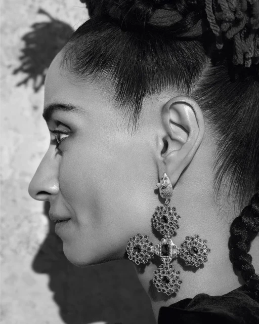 Profile of adult woman with braided hair wearing cross earrings in a studio with a textured backdrop in black and white.