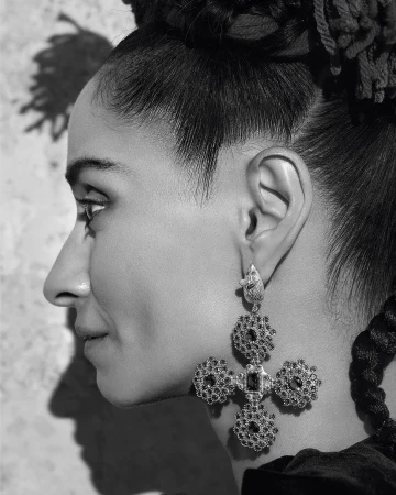 Profile of adult woman with braided hair wearing cross earrings in a studio with a textured backdrop in black and white.
