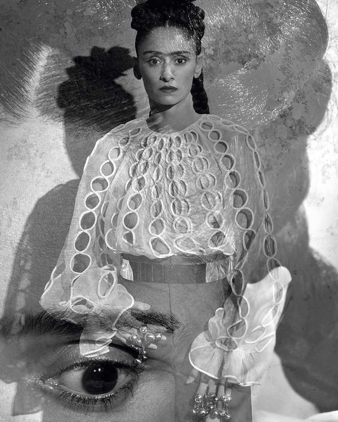Monochromatic portrait of an adult woman with braided hair, wearing an ornate white blouse, contrasted with an oversized eye and shadow.