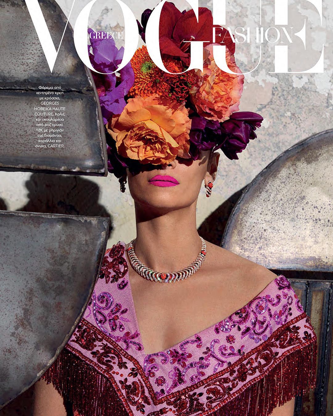 Vogue Greece cover featuring a woman adorned with colorful flowers, wearing an ornate necklace and patterned shawl with fringe.