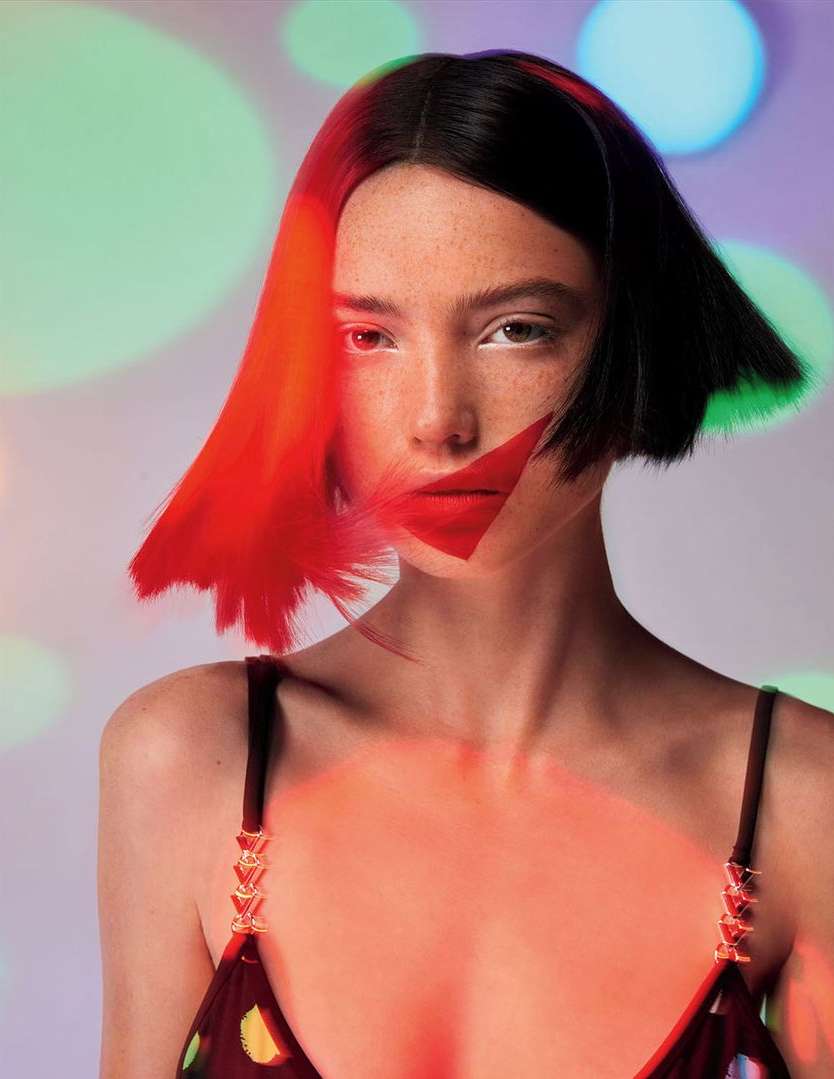 Portrait of a model with dark hair and red lipstick, posing in front of a light background with colorful circles, studio lighting, and artistic flair.