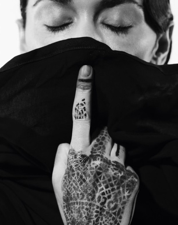Monochromatic portrait of a person with eyes closed, part of their face covered by a fabric with patterned henna tattoo on hand.