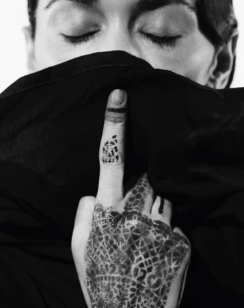 Monochromatic portrait of a person with eyes closed, part of their face covered by a fabric with patterned henna tattoo on hand.