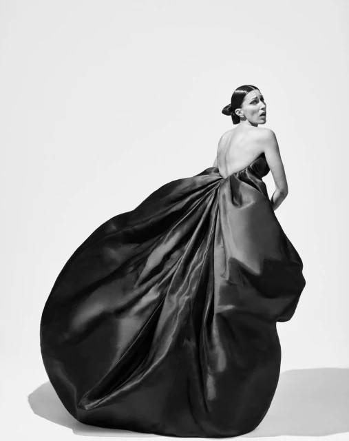 Elegant woman in a backless evening gown turns her head in a studio shot against a bright white background, showcasing fashion and style.